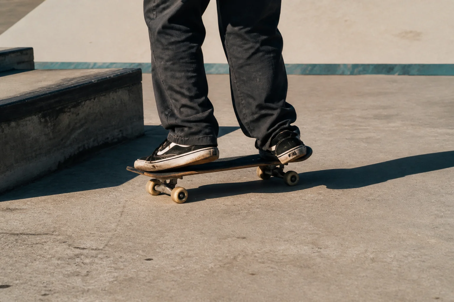 Close-up of a skateboarder's feet rolling beside a sunlit concrete ledge